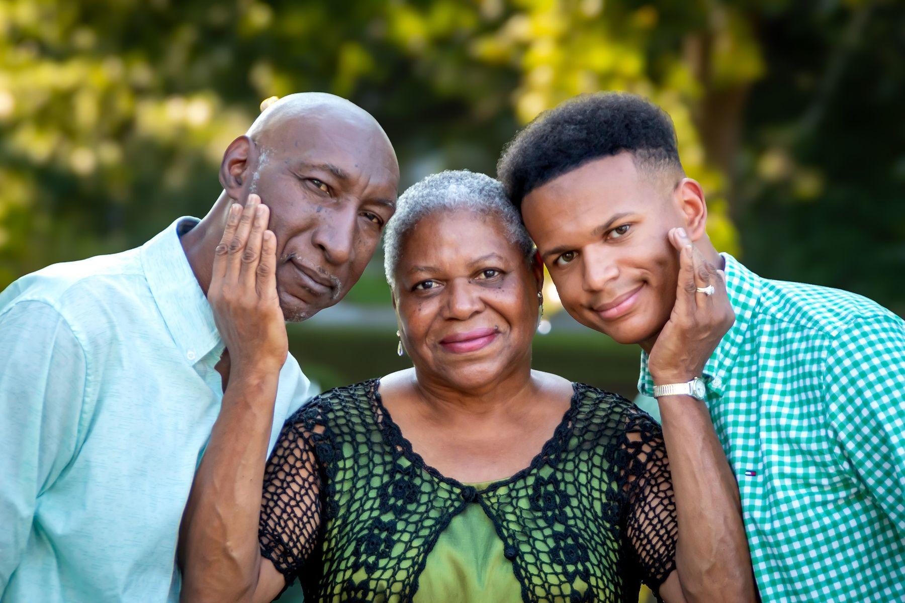 Three people posing closely together outdoors with greenery in the background.