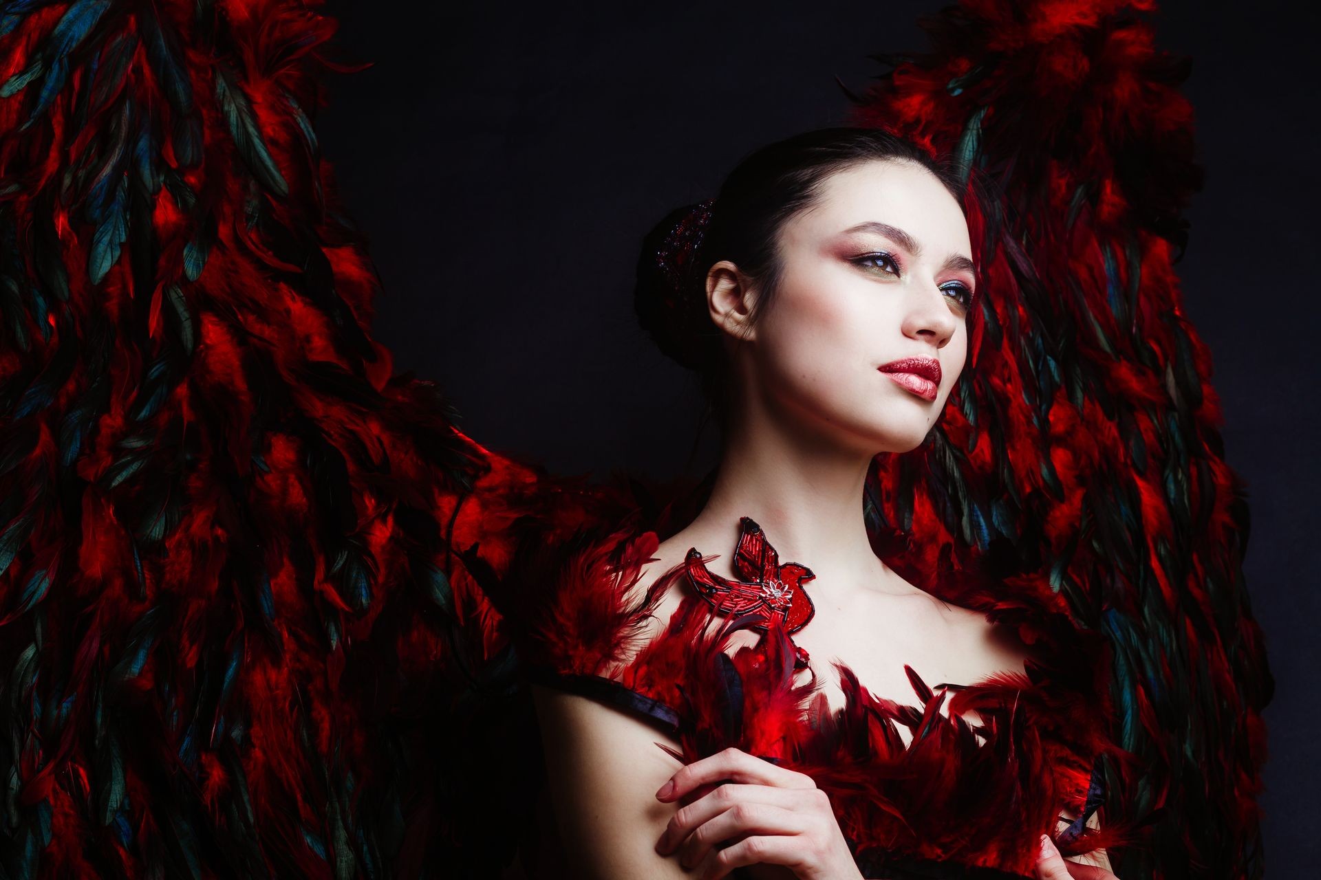 Fashion model brunette covered with feathers and with real angel wings from red feathers behind, fine art photography 